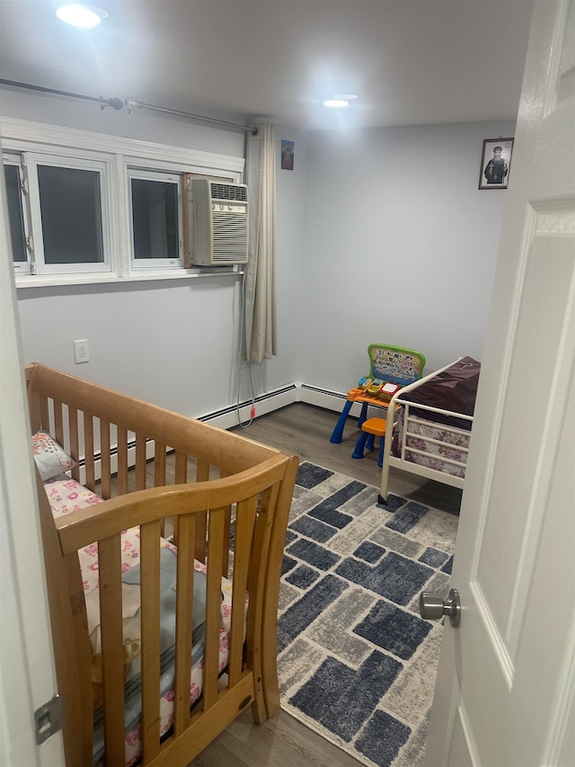 bedroom with dark hardwood / wood-style flooring, baseboard heating, and a nursery area