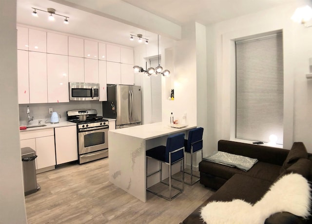 kitchen featuring a breakfast bar, white cabinets, stainless steel appliances, and light wood-style flooring