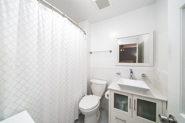bathroom with toilet, tile walls, wainscoting, vanity, and a shower with shower curtain