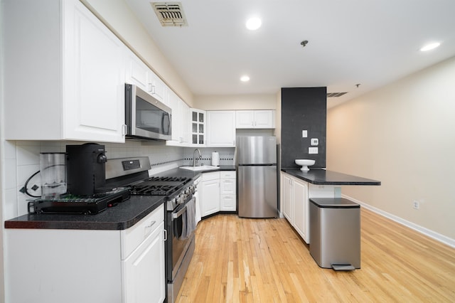 kitchen with stainless steel appliances, a peninsula, light wood-type flooring, decorative backsplash, and recessed lighting