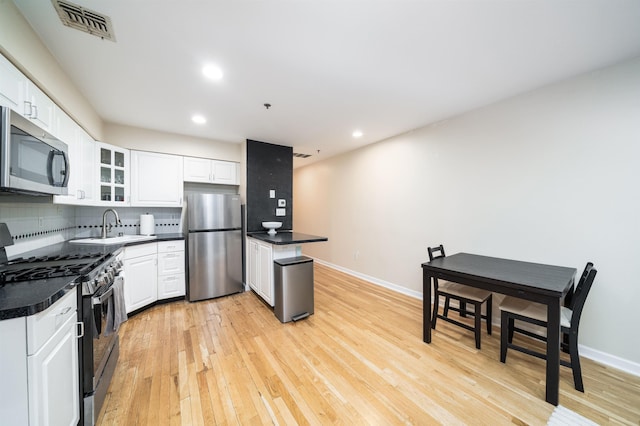kitchen featuring appliances with stainless steel finishes, a sink, light wood-style floors, backsplash, and dark countertops