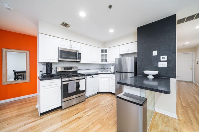 kitchen with appliances with stainless steel finishes, light wood-style flooring, white cabinets, glass insert cabinets, and recessed lighting