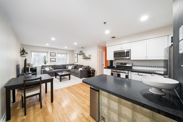 kitchen featuring stainless steel appliances, white cabinets, light wood-style flooring, decorative backsplash, and dark countertops