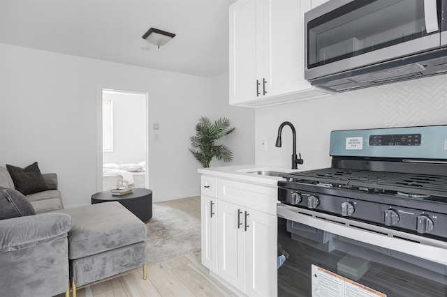 kitchen with stainless steel appliances, sink, white cabinets, and light hardwood / wood-style floors