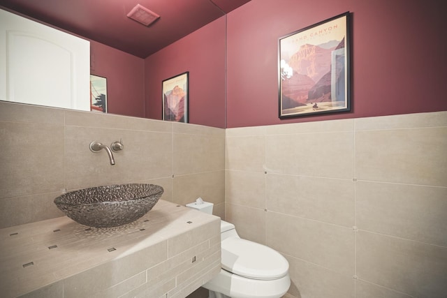 bathroom with toilet, sink, and tile walls