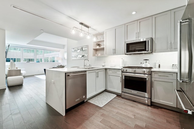 kitchen featuring appliances with stainless steel finishes, pendant lighting, sink, backsplash, and kitchen peninsula