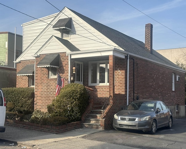 view of front of home featuring roof with shingles, a chimney, and brick siding