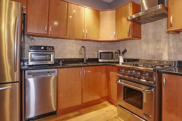 1034 Clinton St Unit 208, Hoboken, NJ 07030 - kitchen featuring appliances with stainless steel finishes, wall chimney exhaust hood, light wood finished floors, dark stone countertops, and backsplash