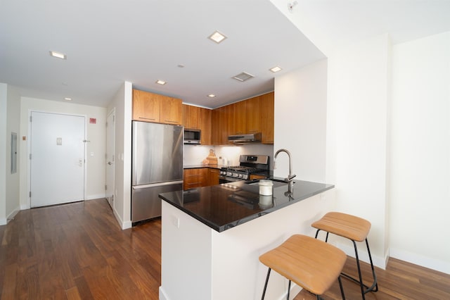 kitchen with sink, a breakfast bar area, kitchen peninsula, stainless steel appliances, and dark wood-type flooring