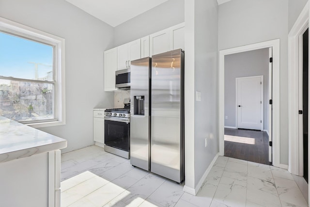 kitchen featuring stainless steel appliances, marble finish floor, white cabinets, and baseboards