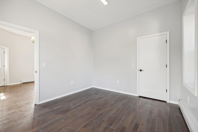 spare room featuring dark wood-type flooring, baseboard heating, and baseboards