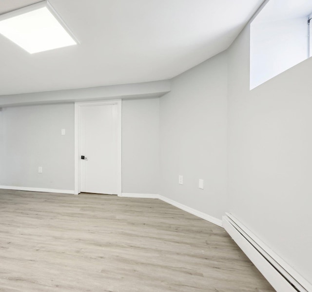 basement featuring light wood-type flooring, baseboards, and baseboard heating