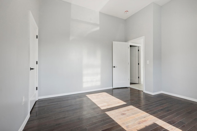 empty room with a high ceiling, baseboards, and wood finished floors