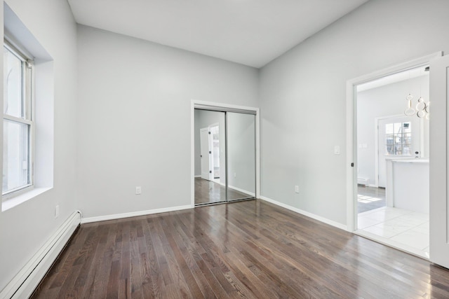 unfurnished bedroom with a closet, baseboards, baseboard heating, and wood finished floors