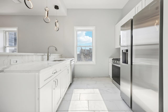 kitchen with light stone counters, marble finish floor, stainless steel appliances, white cabinetry, and a sink