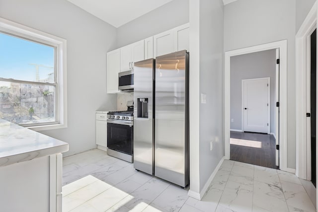 kitchen featuring marble finish floor, stainless steel appliances, white cabinetry, and baseboards