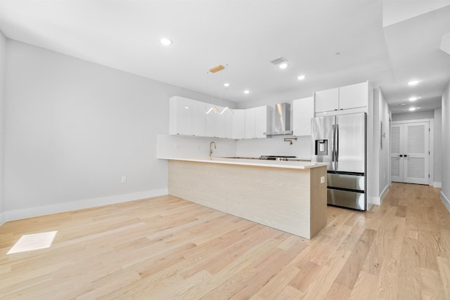 kitchen with pendant lighting, white cabinetry, stainless steel fridge with ice dispenser, kitchen peninsula, and wall chimney exhaust hood