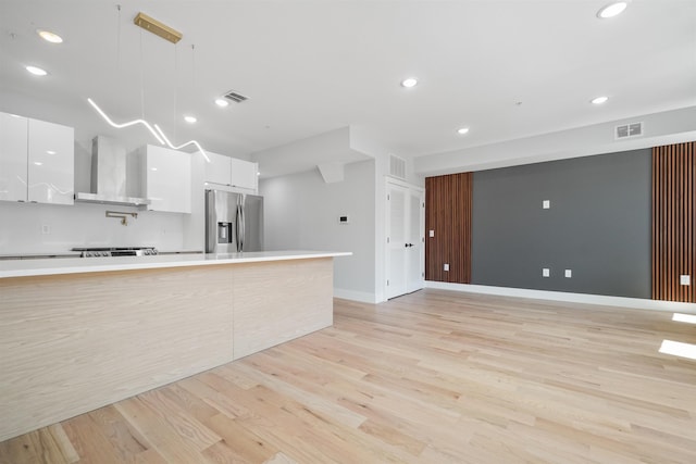 kitchen with white cabinetry, hanging light fixtures, wall chimney range hood, and stainless steel refrigerator with ice dispenser