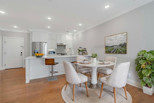 dining area with sink, crown molding, and light hardwood / wood-style flooring