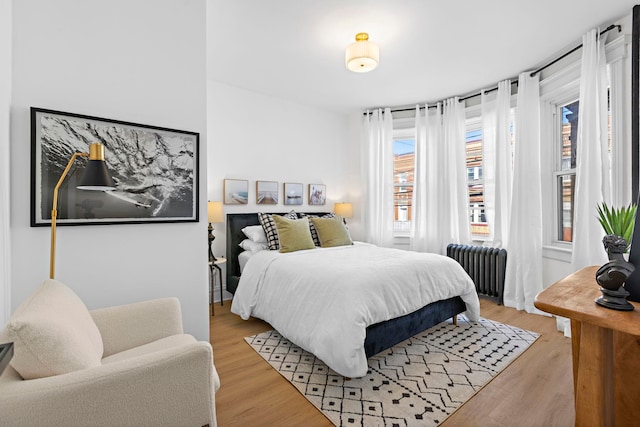 bedroom featuring light wood-style flooring, radiator heating unit, and multiple windows