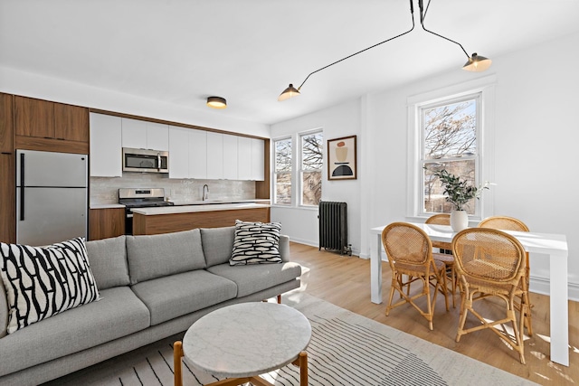 living area featuring baseboards, radiator heating unit, and light wood-style flooring