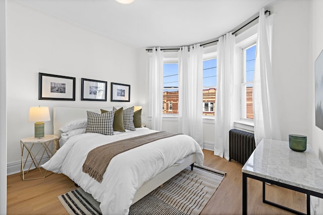 bedroom featuring multiple windows, radiator, and light wood-style floors