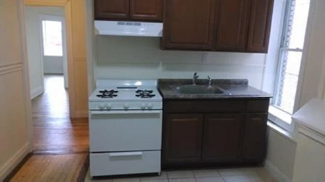 kitchen with dark brown cabinetry, sink, white range with gas cooktop, light hardwood / wood-style flooring, and exhaust hood