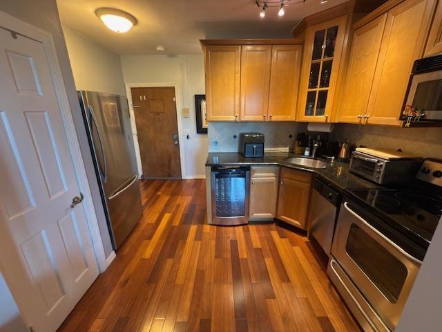108 Waldo Ave Unit 4A, Jersey City, NJ 07306 - kitchen featuring stainless steel appliances, dark countertops, dark wood-style flooring, glass insert cabinets, and backsplash