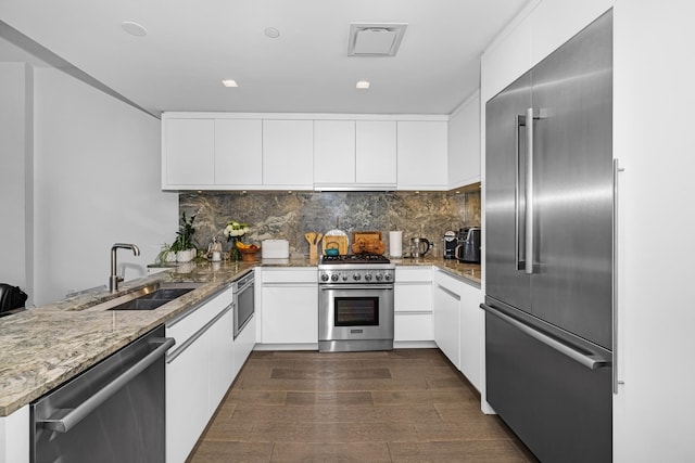 kitchen with light stone countertops, sink, premium appliances, dark hardwood / wood-style floors, and white cabinets