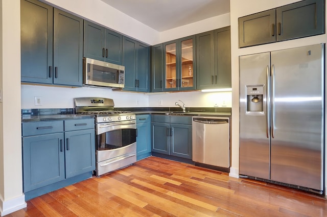 389 Washington St Unit 30C, Jersey City, NJ 07302 - kitchen featuring stainless steel appliances, dark countertops, light wood-style floors, and glass insert cabinets