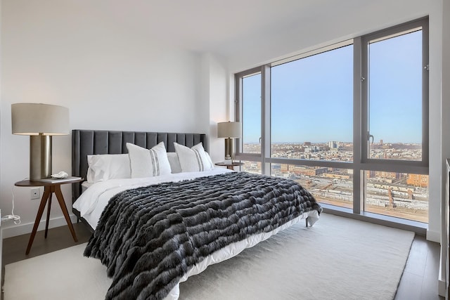 bedroom with baseboards, floor to ceiling windows, wood finished floors, and a city view