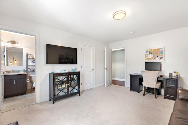 office area featuring baseboards, a sink, and light colored carpet