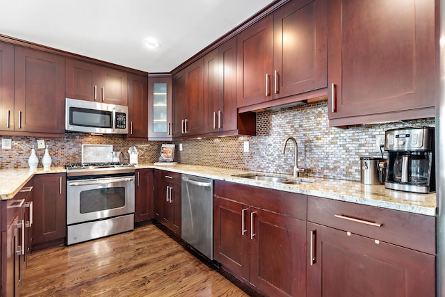 kitchen featuring appliances with stainless steel finishes, a sink, light stone counters, and wood finished floors