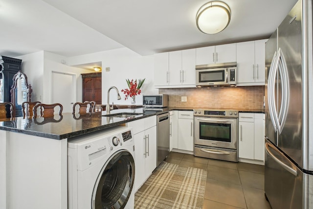 kitchen featuring dark tile patterned flooring, a sink, washer / clothes dryer, appliances with stainless steel finishes, and a peninsula