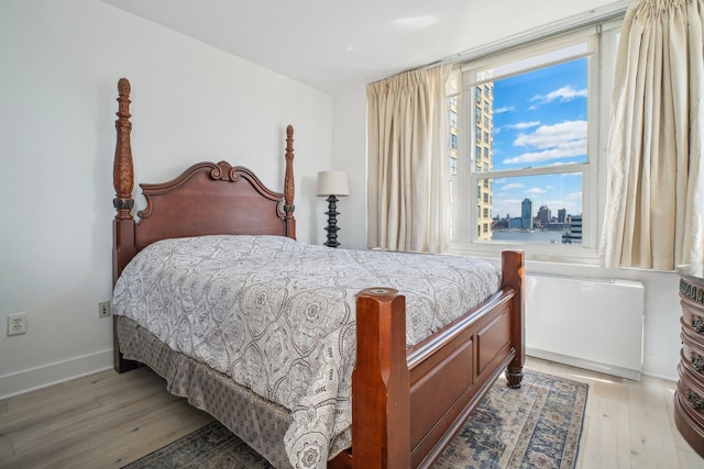 bedroom with a view of city, light wood-style flooring, and baseboards