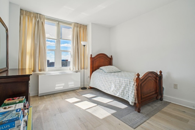 bedroom featuring baseboards, wood finished floors, and radiator heating unit