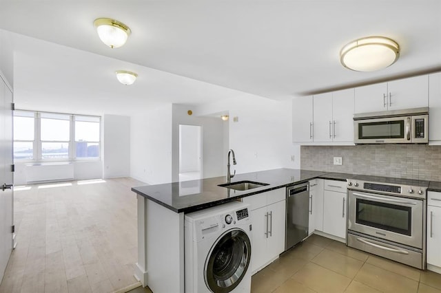 kitchen featuring open floor plan, washer / dryer, a peninsula, stainless steel appliances, and a sink