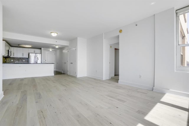 unfurnished living room with baseboards, light wood-type flooring, and a wealth of natural light