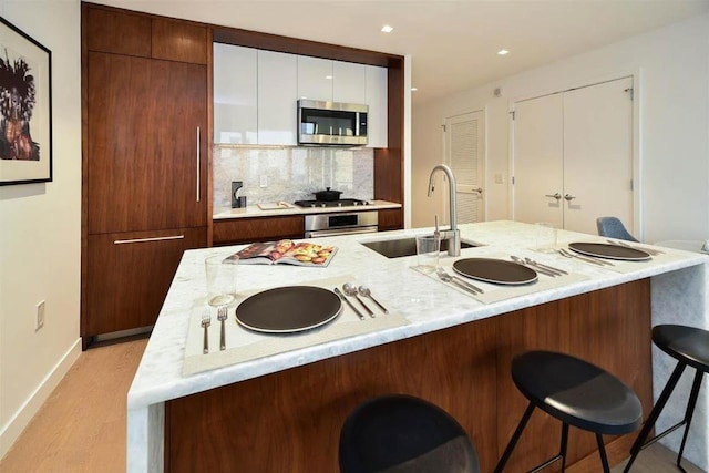 kitchen featuring appliances with stainless steel finishes, light wood-type flooring, backsplash, a kitchen island with sink, and sink