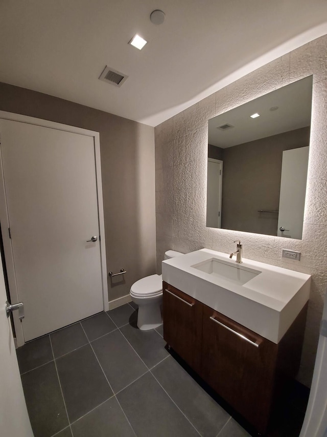 half bathroom featuring a textured wall, tile patterned flooring, toilet, vanity, and visible vents