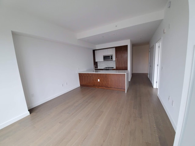 unfurnished living room with a sink, light wood-style flooring, and baseboards