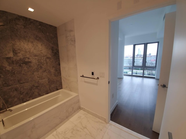 full bathroom with marble finish floor, a washtub, and baseboards