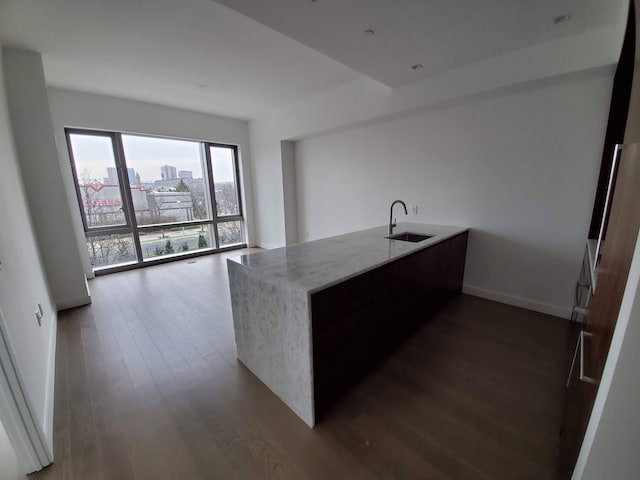 kitchen featuring a city view, dark wood finished floors, a sink, light stone countertops, and baseboards