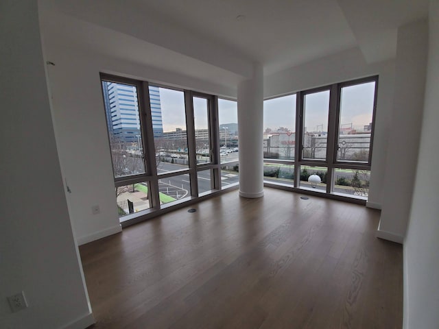 unfurnished room featuring a view of city, baseboards, and wood finished floors