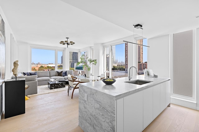 kitchen with white cabinetry, sink, light hardwood / wood-style flooring, kitchen peninsula, and decorative light fixtures