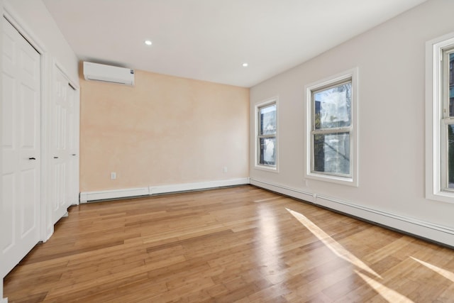 unfurnished bedroom with baseboard heating, a wall mounted air conditioner, and light wood finished floors