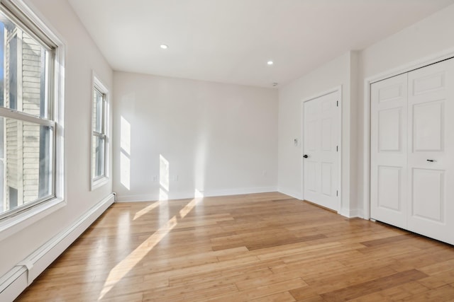 interior space featuring light wood-type flooring, a baseboard radiator, a healthy amount of sunlight, and baseboards