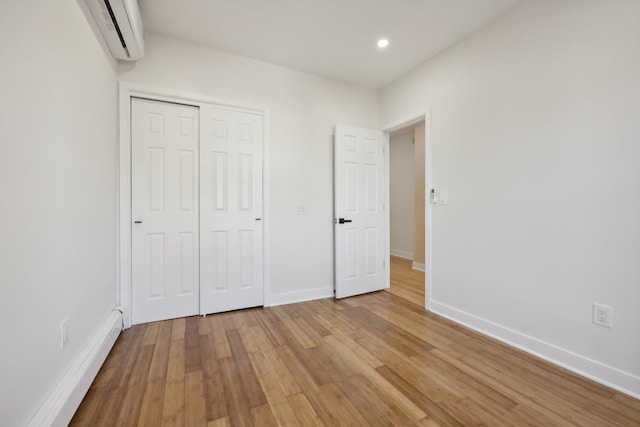 unfurnished bedroom featuring a baseboard heating unit, light wood-type flooring, a wall unit AC, and baseboards