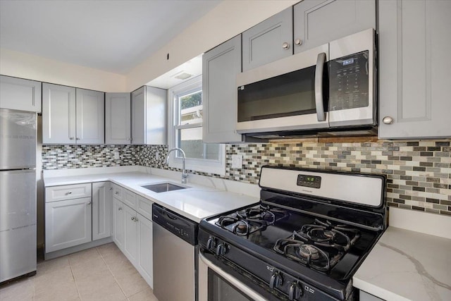 kitchen featuring stainless steel appliances, sink, tasteful backsplash, light tile patterned floors, and gray cabinets