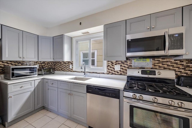 kitchen featuring stainless steel appliances, decorative backsplash, sink, gray cabinetry, and light tile patterned flooring